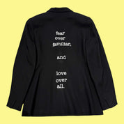 Blue Greenie black blazer featuring white vinyl quote text on the back against a yellow background