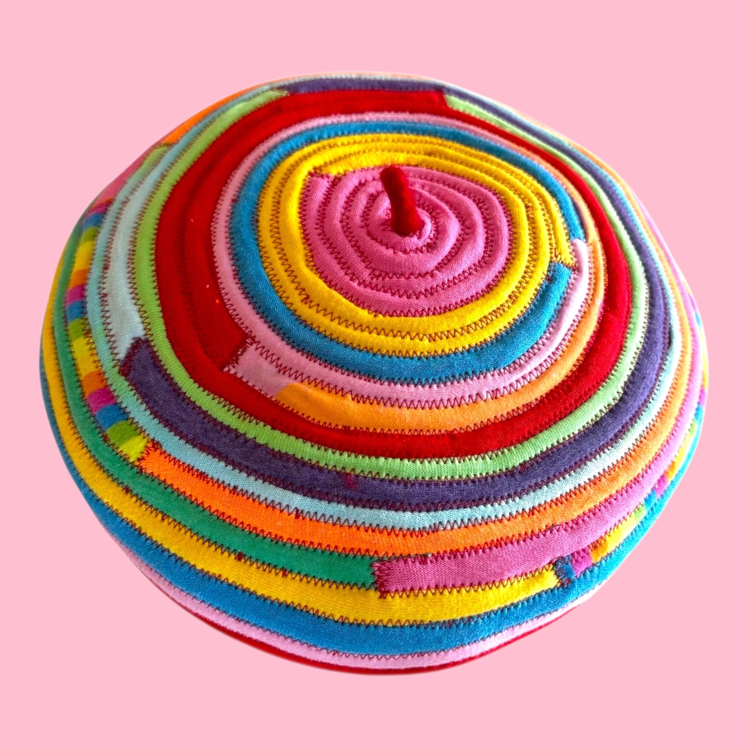 Blue Greenie red wool beret featuring a vibrant spiral pattern made from colorful sewn t-shirt fabric strips.